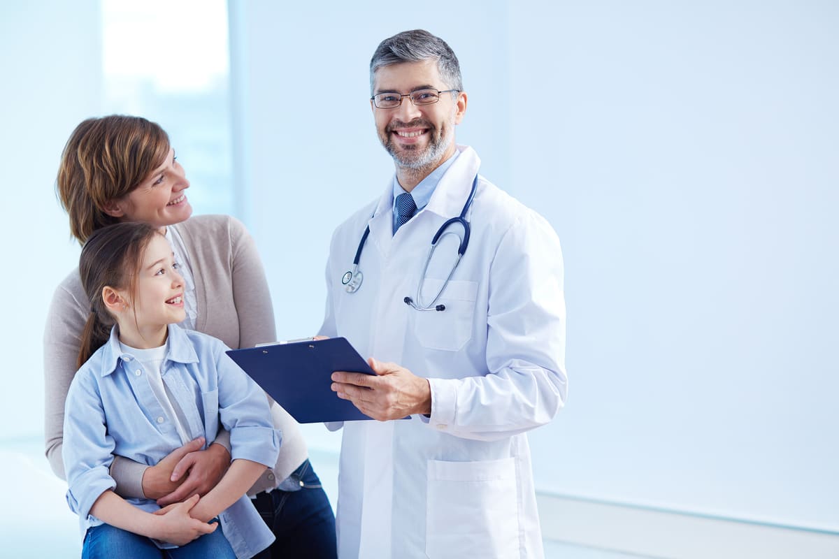 A imagem mostra um médico sorridente, segurando uma prancheta, ao lado de uma mulher que segura uma criança nos braços. A cena transmite confiança e bem-estar, destacando a relação positiva entre o profissional de saúde e os pacientes. Em contextos como este, é importante entender o que é cobertura parcial temporária. Trata-se de uma restrição aplicada por planos de saúde, onde a cobertura de procedimentos relacionados a doenças ou lesões preexistentes é limitada por um período determinado. Isso significa que, por um tempo, certos tratamentos podem não ser cobertos pelo plano, mas após esse período, a cobertura completa é restabelecida.